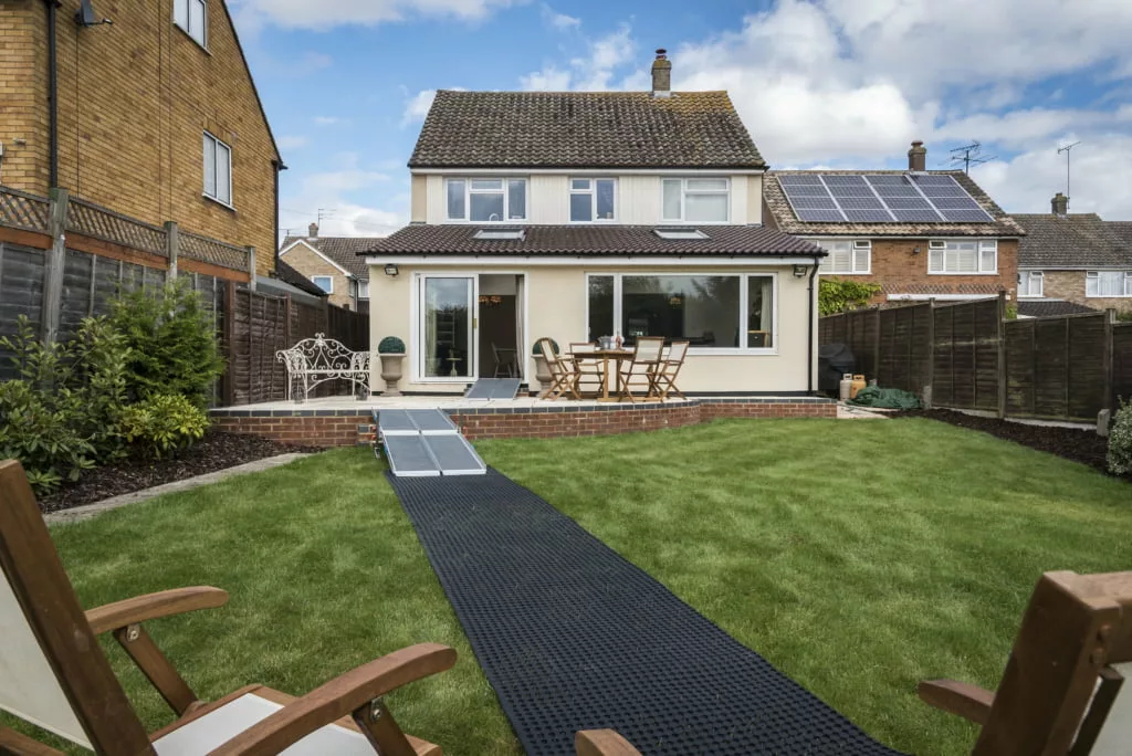 house with a lawned garden and a rolled out track for a mobility scooter to drive over