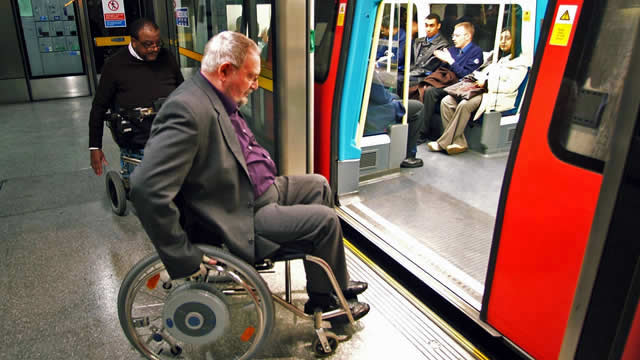 an older man in a wheelchair, about to get on a tube train