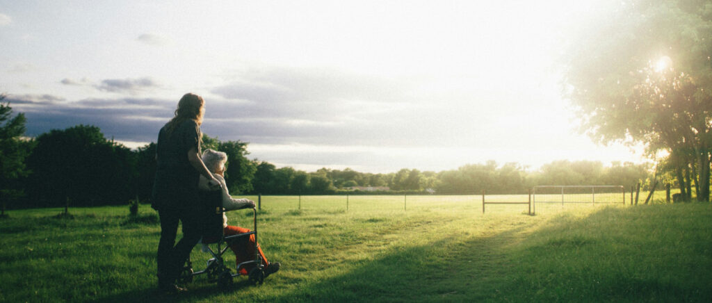 Women being pushed in a wheelchair across a grassy field