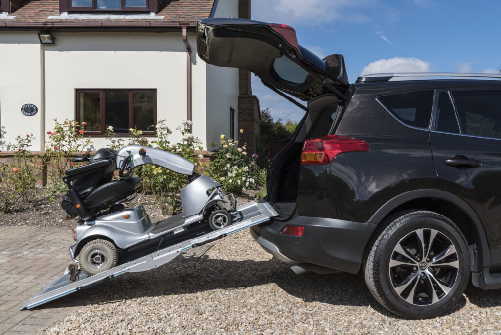A mobility scooter being lifted into a car boot with a ramp