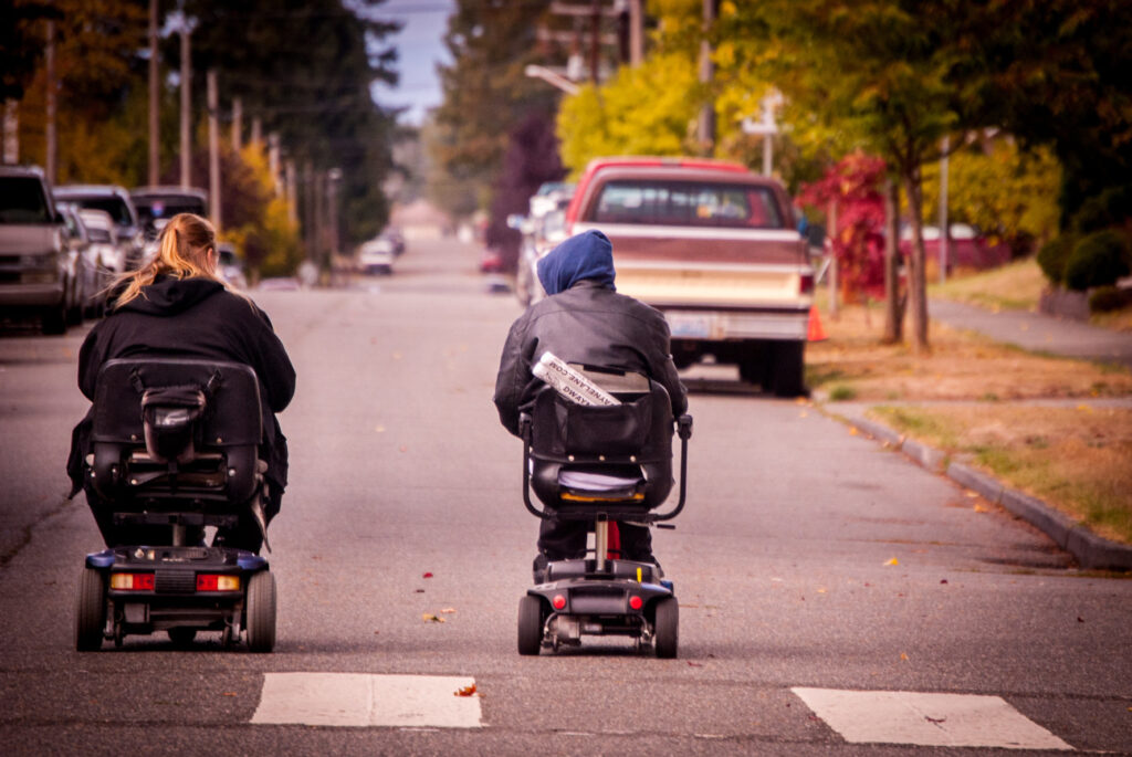 Two people riding a mobility scooter on the road