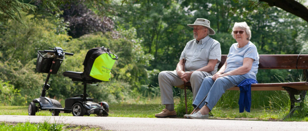 A mobility scooter in the park with a couple sitting on a bench
