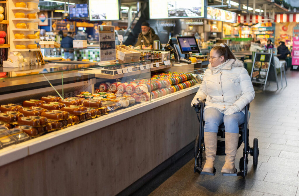 a lady in a powerchair looking at cheese and meats in a market