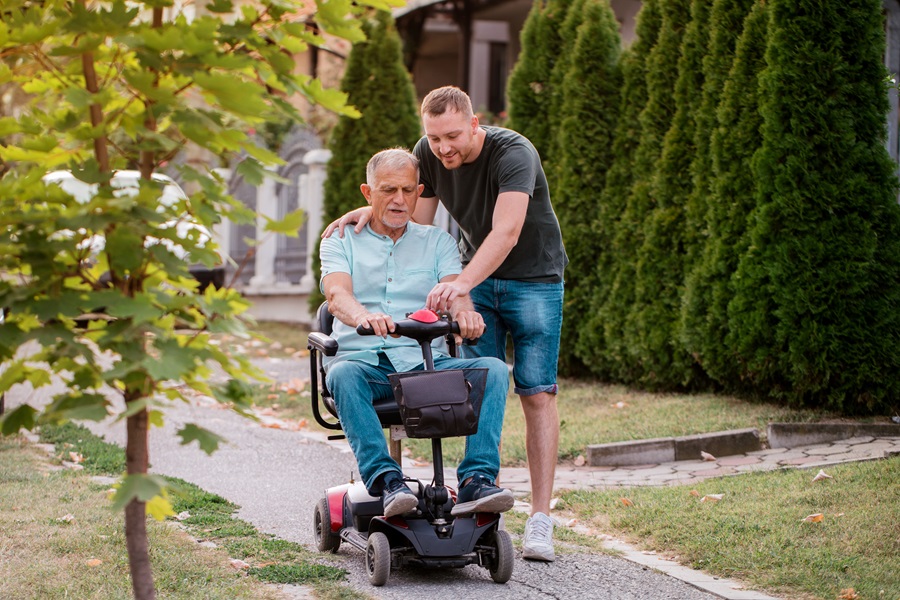 Young man on a path showing an older man how to use his mobility scooter
