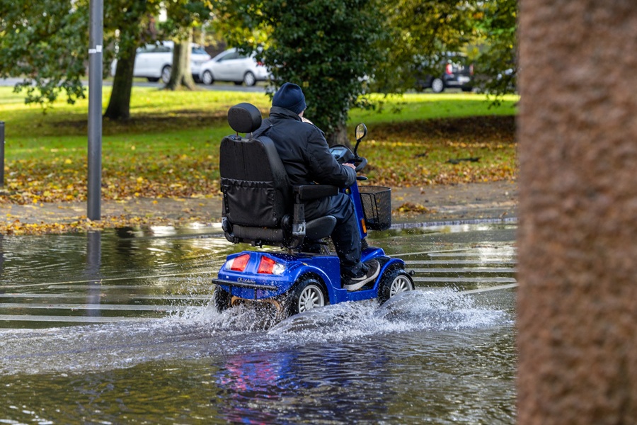 Man riding a blue mobility scooter through a large puddle in the rain