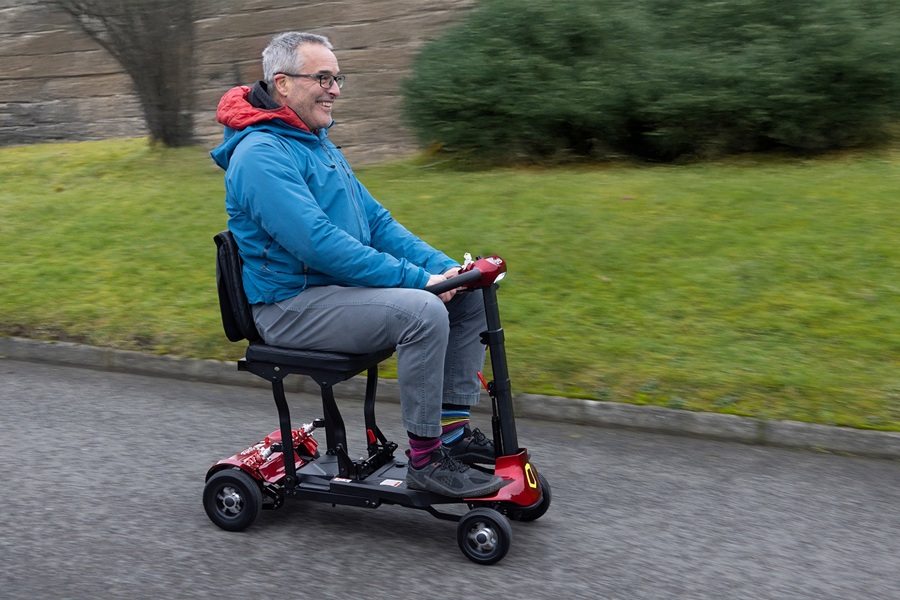 Man on a red mobility scooter driving along a pavement